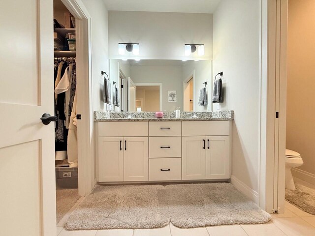 bathroom with double vanity, toilet, a walk in closet, tile patterned floors, and a sink