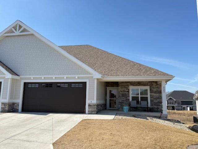 craftsman house featuring a garage, driveway, stone siding, and a shingled roof