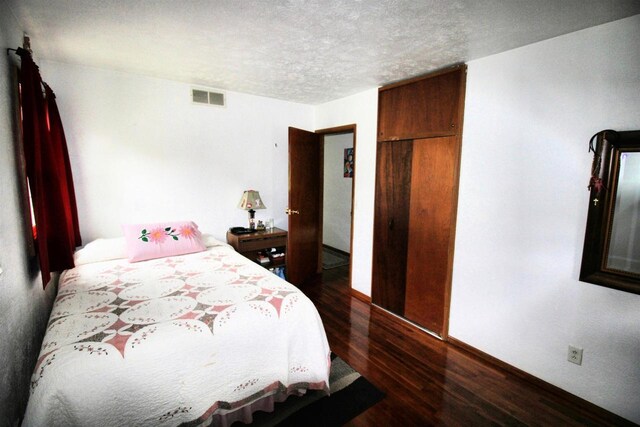 bedroom featuring baseboards, dark wood-type flooring, a textured ceiling, and visible vents