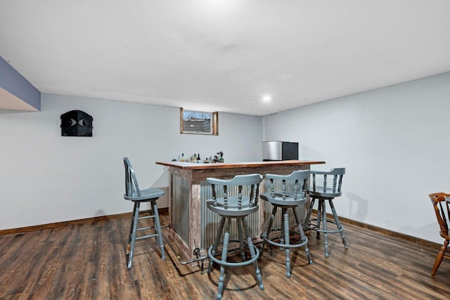 bar featuring baseboards, a bar, and wood finished floors