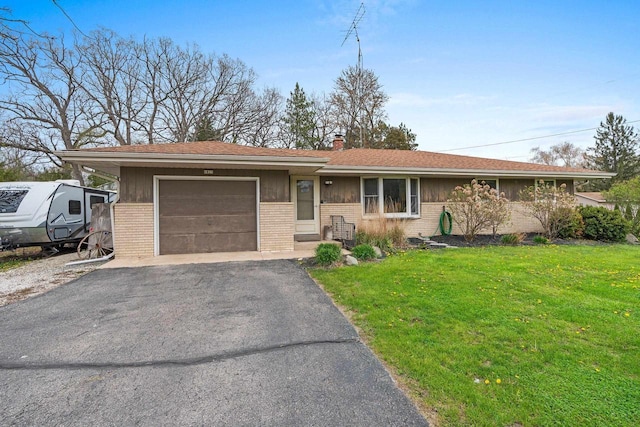 ranch-style home with a front yard, a chimney, brick siding, an attached garage, and driveway