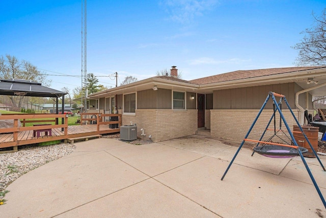 back of house featuring a gazebo, brick siding, a deck, a chimney, and central air condition unit