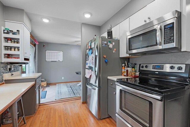 kitchen featuring baseboards, light countertops, white cabinets, light wood finished floors, and stainless steel appliances