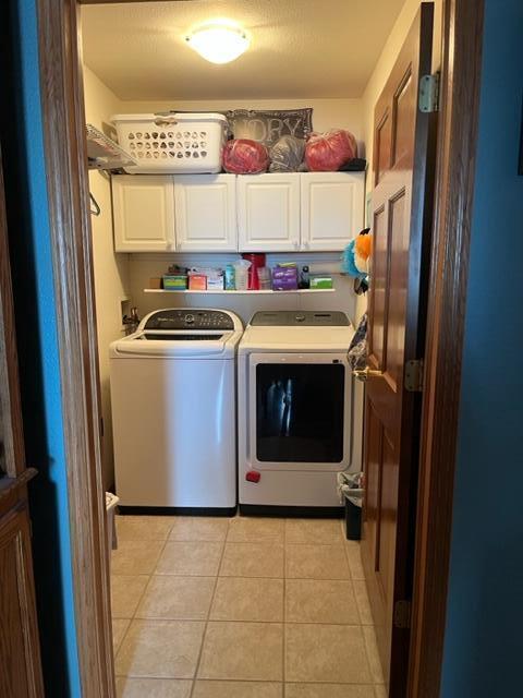 laundry room with light tile patterned flooring, cabinet space, and washer and clothes dryer