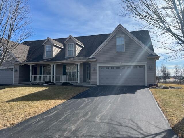 cape cod home with a garage, covered porch, driveway, and a front yard