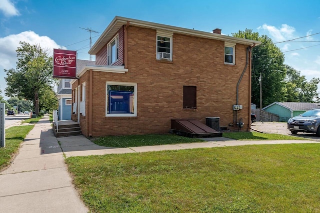 view of side of property featuring a chimney, a yard, central AC, and brick siding