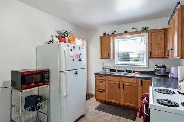 kitchen with a sink, dark countertops, brown cabinets, and white appliances