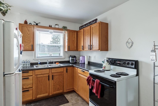 kitchen featuring brown cabinetry, electric range, dark countertops, a sink, and freestanding refrigerator