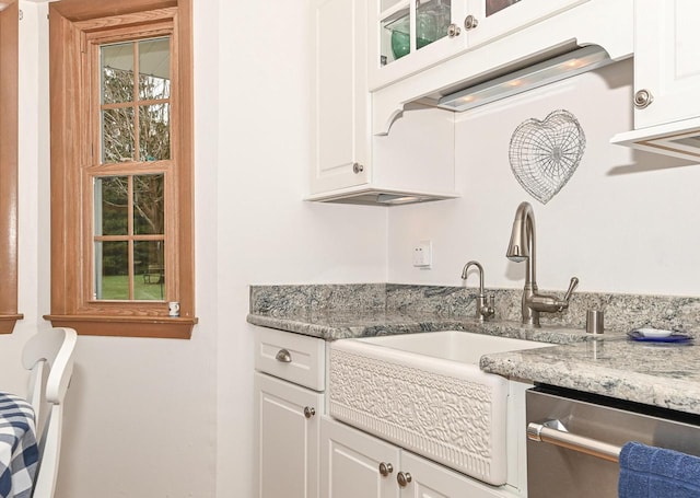 interior space with glass insert cabinets, light stone counters, white cabinets, and dishwasher