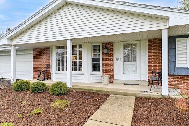 entrance to property featuring a porch, brick siding, and a garage