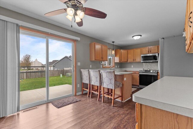 kitchen featuring a kitchen bar, dark wood-type flooring, light countertops, plenty of natural light, and appliances with stainless steel finishes