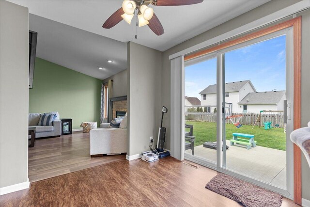 interior space with wood finished floors, a fireplace, baseboards, ceiling fan, and vaulted ceiling