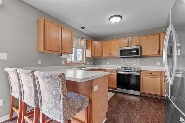 kitchen with dark wood-style flooring, a sink, light countertops, stainless steel appliances, and a peninsula
