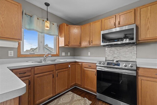 kitchen with dark wood-type flooring, light countertops, a sink, hanging light fixtures, and stainless steel appliances