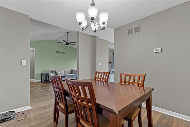 dining space featuring vaulted ceiling, ceiling fan with notable chandelier, wood finished floors, and visible vents