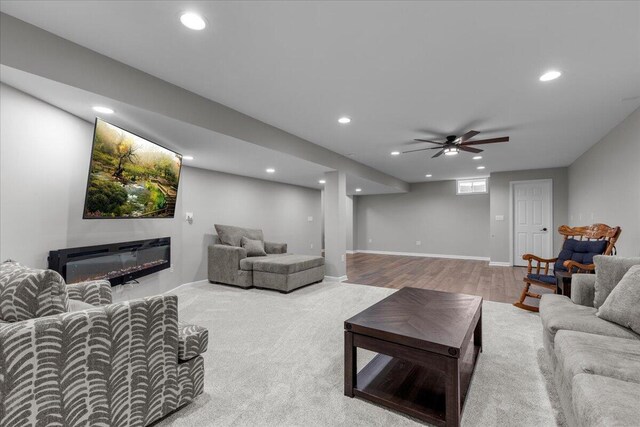 living area featuring a glass covered fireplace, wood finished floors, baseboards, recessed lighting, and a ceiling fan