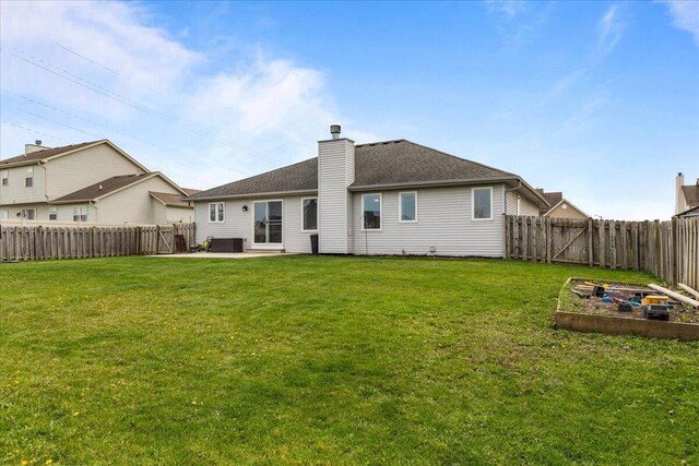 back of house featuring a fenced backyard, a vegetable garden, a chimney, a patio area, and a lawn
