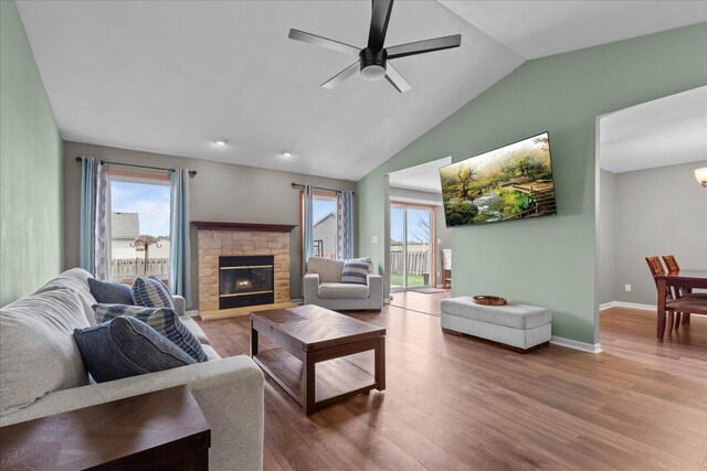 living room featuring a stone fireplace, a ceiling fan, baseboards, wood finished floors, and lofted ceiling