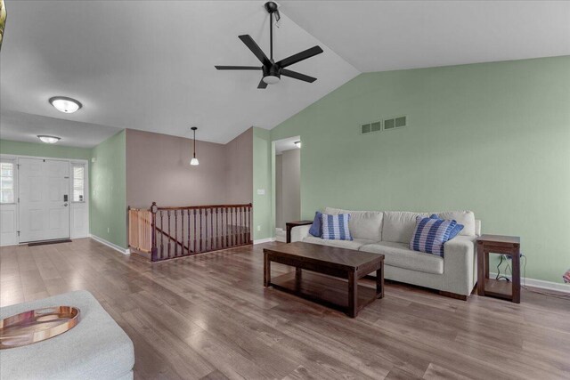 living area with visible vents, wood finished floors, baseboards, ceiling fan, and vaulted ceiling