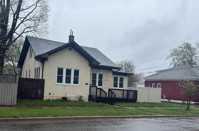 bungalow-style house with stucco siding, roof with shingles, fence, and a chimney