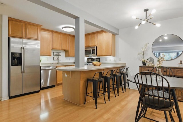 kitchen with a breakfast bar area, a peninsula, an inviting chandelier, stainless steel appliances, and light wood-style flooring