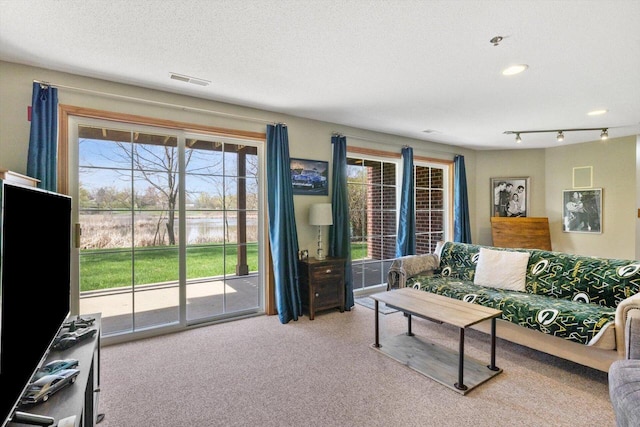 carpeted living room featuring visible vents, rail lighting, a textured ceiling, and a water view