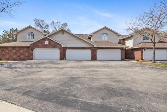view of front of house with an attached garage, roof with shingles, driveway, and brick siding