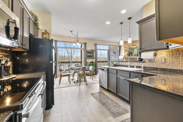 kitchen with appliances with stainless steel finishes, a sink, a peninsula, decorative light fixtures, and decorative backsplash