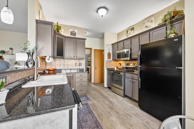 kitchen with backsplash, a sink, dark stone countertops, stainless steel appliances, and light wood-style flooring