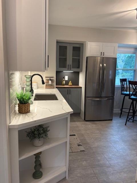 kitchen with open shelves, a sink, light stone counters, freestanding refrigerator, and glass insert cabinets