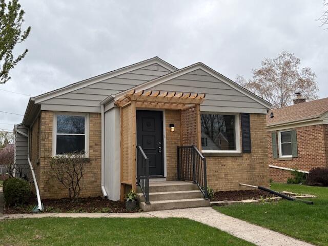 bungalow featuring brick siding, a front lawn, and a pergola