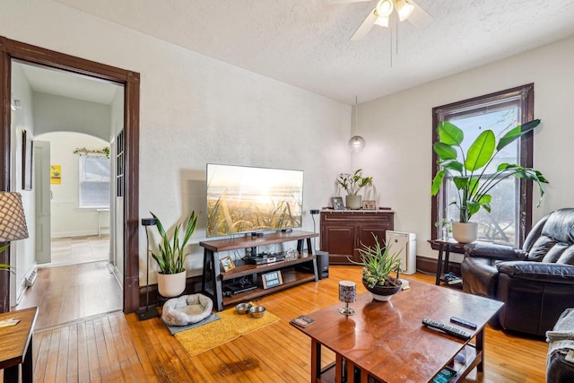 living area with ceiling fan, wood-type flooring, arched walkways, a textured ceiling, and baseboards