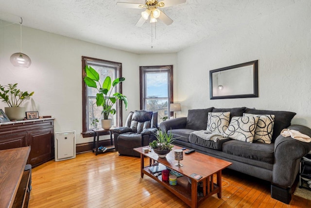 living room featuring a ceiling fan, a textured ceiling, and light wood-style flooring