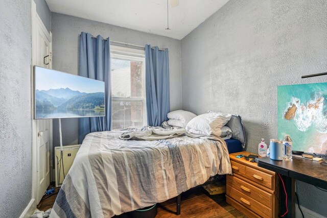 bedroom with a ceiling fan, a textured wall, and wood finished floors