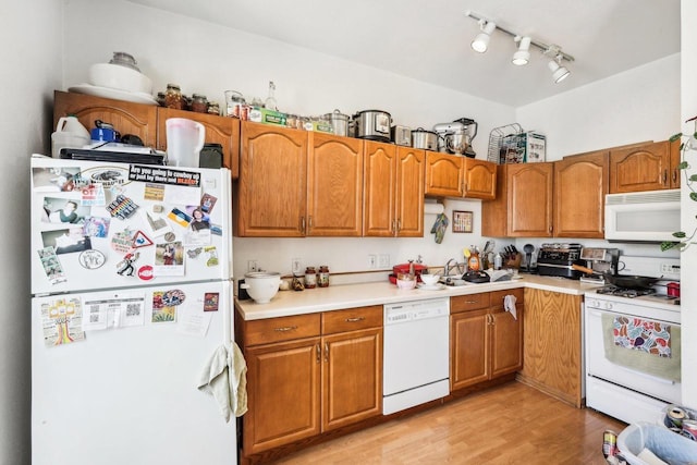 kitchen with track lighting, brown cabinetry, white appliances, light countertops, and light wood finished floors