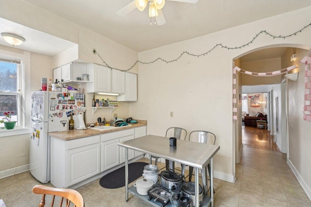kitchen featuring freestanding refrigerator, baseboards, white cabinetry, arched walkways, and a ceiling fan
