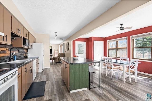kitchen featuring dark countertops, a sink, baseboards, dark wood-style floors, and white appliances