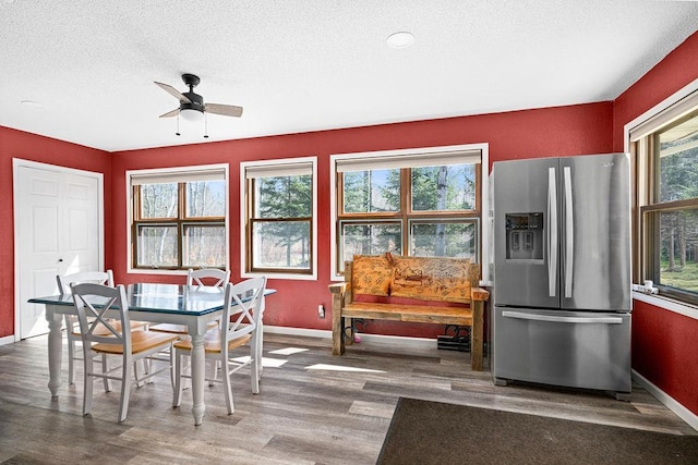 dining space with a textured ceiling, baseboards, ceiling fan, and wood finished floors