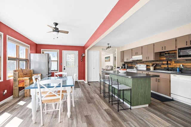 kitchen featuring dark wood-style flooring, white appliances, under cabinet range hood, a sink, and gray cabinetry
