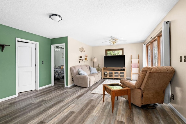living area featuring baseboards, a ceiling fan, a textured ceiling, and wood finished floors