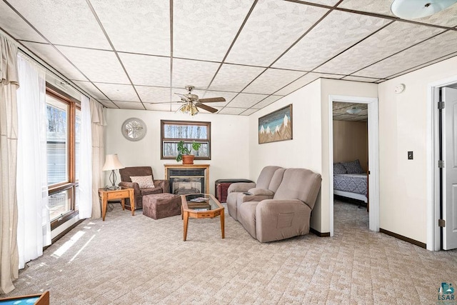 living area featuring a ceiling fan, baseboards, light carpet, and a drop ceiling