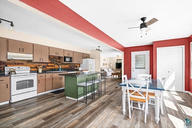 kitchen featuring a kitchen island, dark countertops, white appliances, dark wood-style floors, and under cabinet range hood