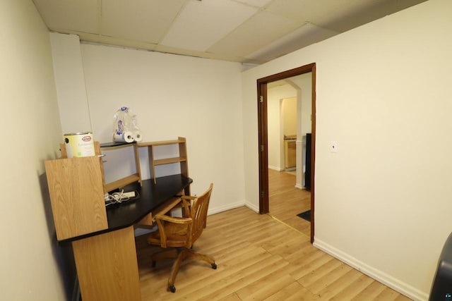 office area with baseboards, a drop ceiling, and light wood-style flooring