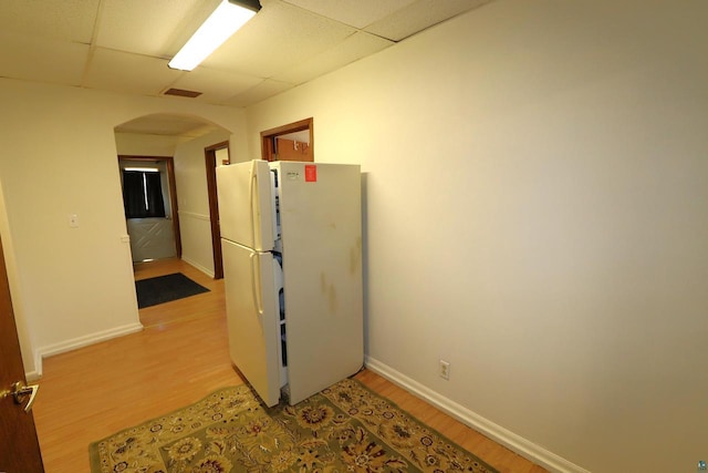 corridor with baseboards, arched walkways, light wood finished floors, and a paneled ceiling