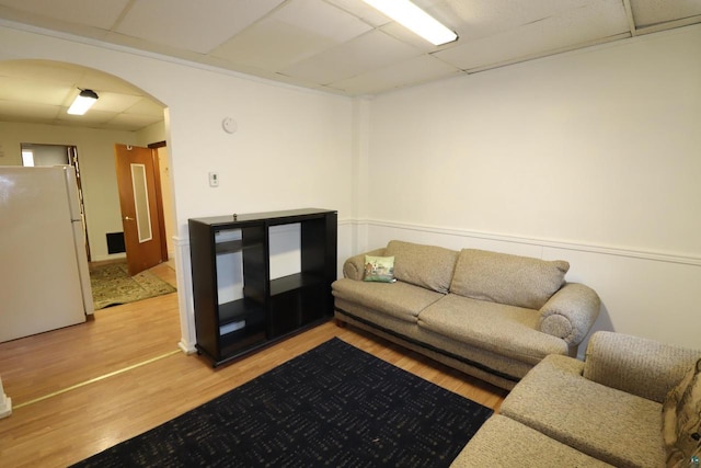 living area featuring arched walkways, light wood-style flooring, and a paneled ceiling