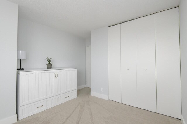 unfurnished bedroom with baseboards, light carpet, and a closet