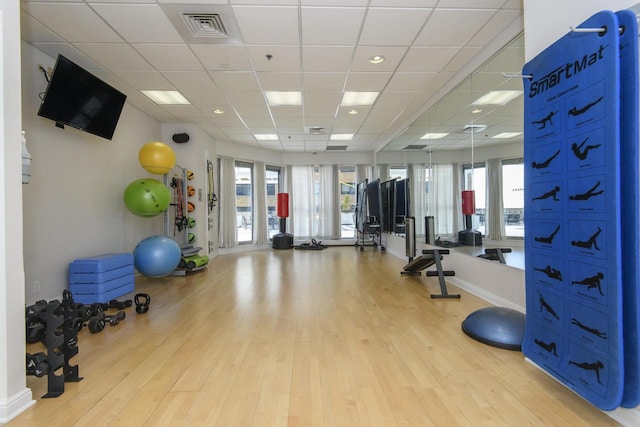exercise room with light wood finished floors, a paneled ceiling, and visible vents