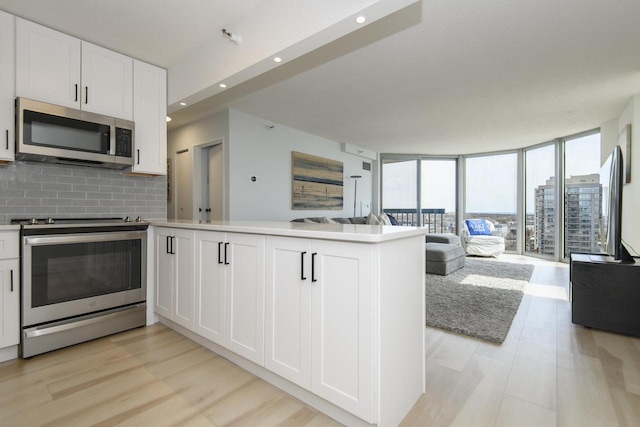 kitchen featuring white cabinets, appliances with stainless steel finishes, a peninsula, open floor plan, and backsplash