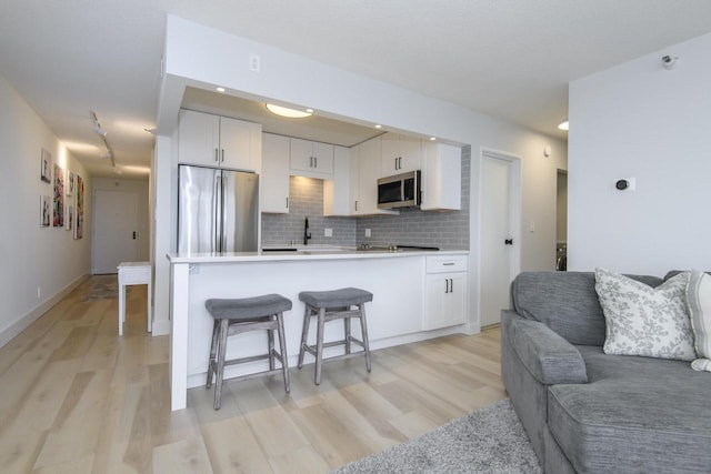 kitchen with a breakfast bar area, appliances with stainless steel finishes, white cabinets, open floor plan, and light wood-style floors