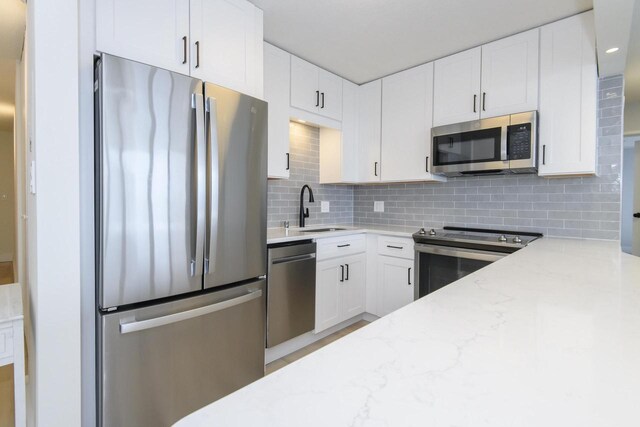 kitchen with light stone countertops, white cabinetry, tasteful backsplash, a sink, and stainless steel appliances
